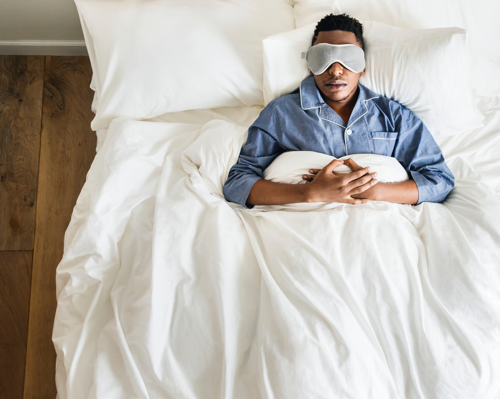 Man asleep in bed with eyemask wearing pyjamas