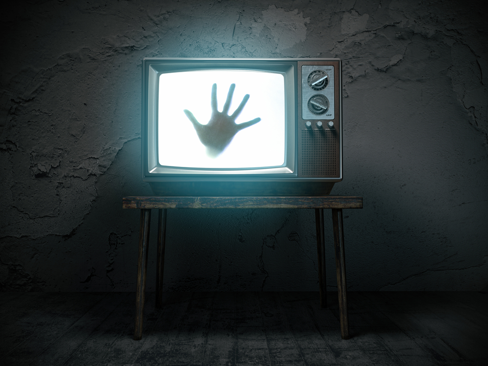 Dirty room with old television playing horror movie showing hand reaching out