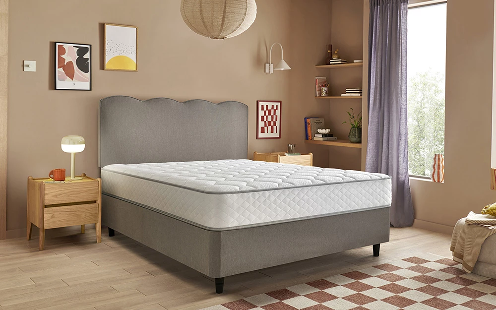 The Silentnight Memory 800 Mirapocket Mattress in a cosy, beige bedroom accented with yellow, red and organce furniture and picture frames.
