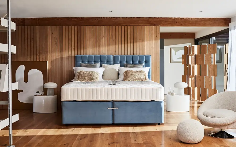 The Sleepeezee Hotel Supreme 1400 Pocket Contract Mattress in a luxurious hotel room on a blue zip and link divan base. The room is accented with wooden walls and white, fluffy furniture.